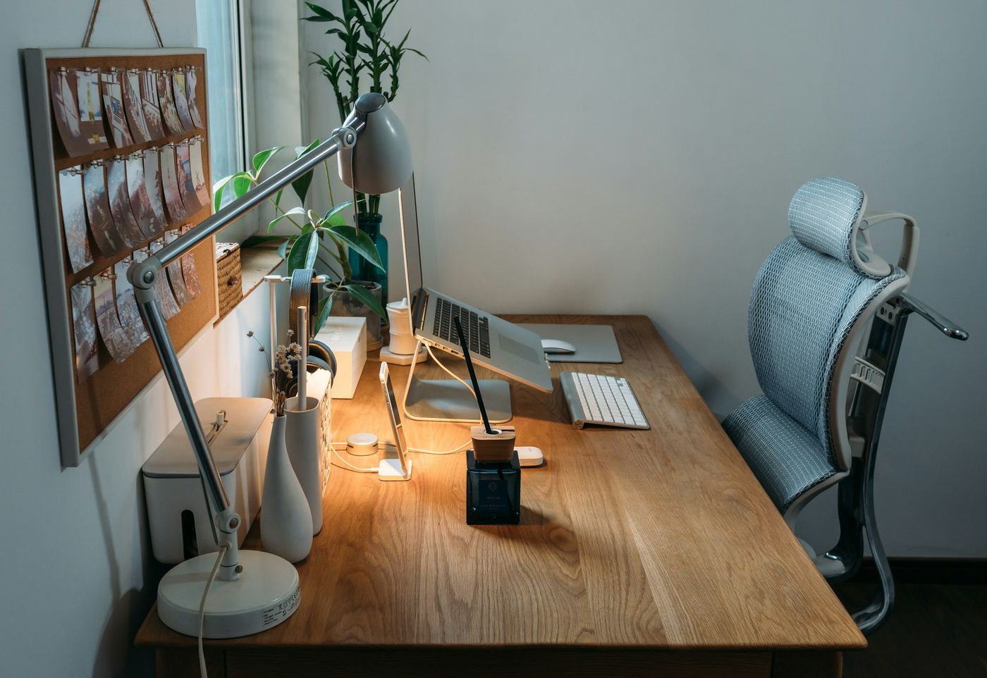 Bureau en bois avec lampe articulée, ordinateur et fauteuil réglable près d'une fenêtre