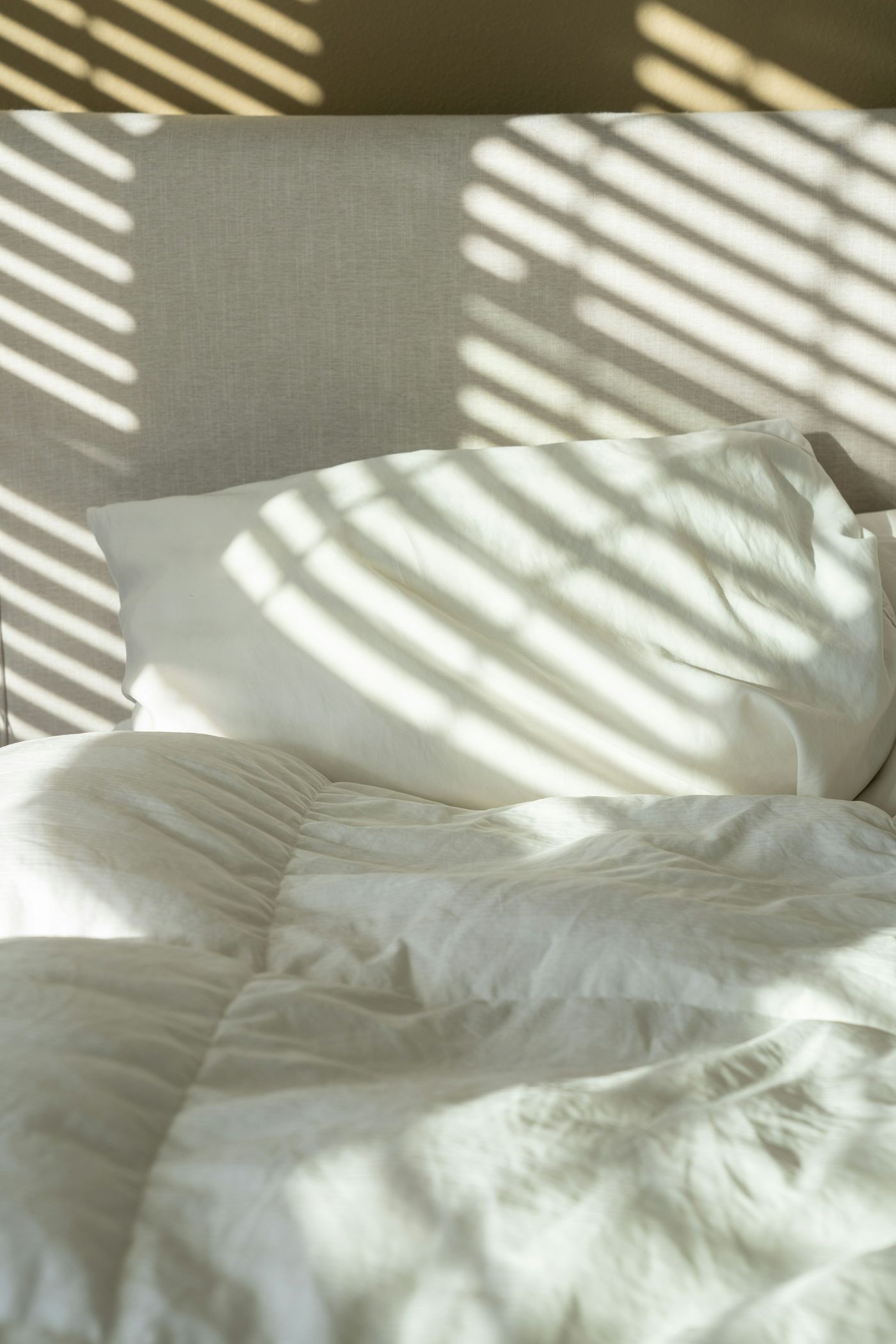 Lit aux draps blancs traversé par la lumière d'un store